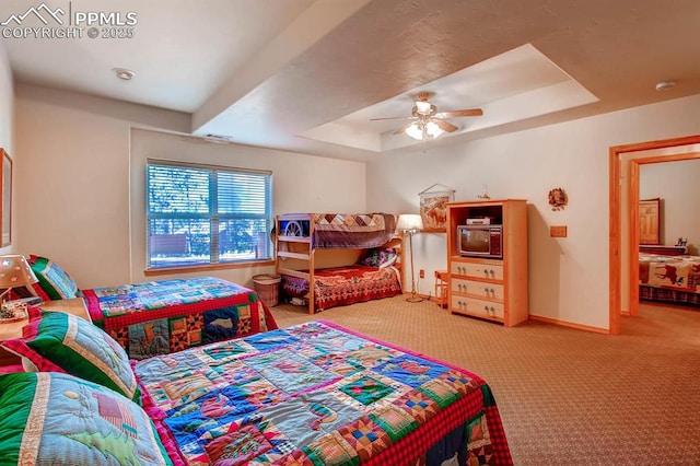 carpeted bedroom with ceiling fan and a tray ceiling