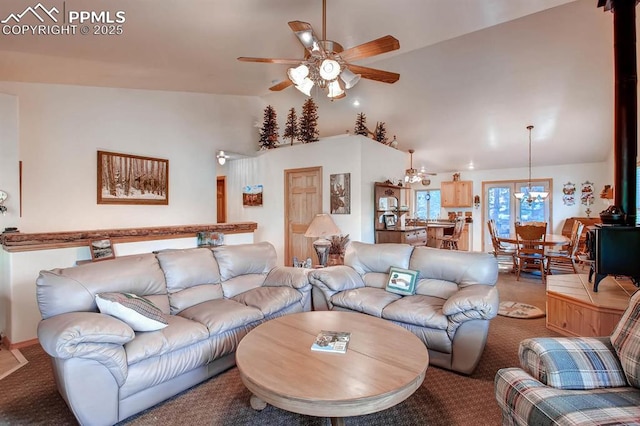 living room featuring ceiling fan with notable chandelier, light colored carpet, vaulted ceiling, and a wood stove