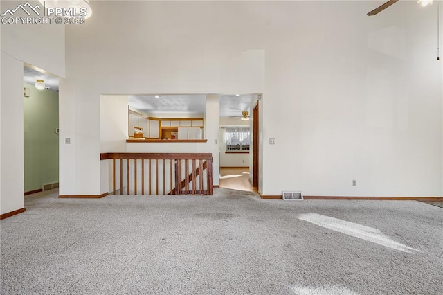 carpeted empty room featuring ceiling fan and a towering ceiling