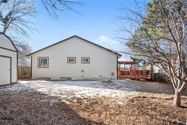 snow covered rear of property with a deck and a storage shed