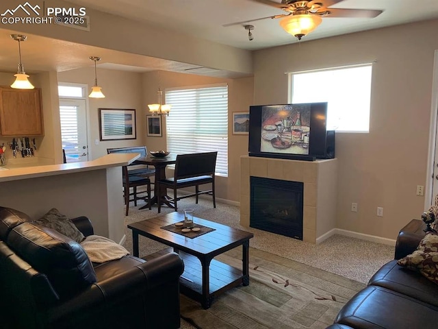 carpeted living room with ceiling fan with notable chandelier and a tile fireplace