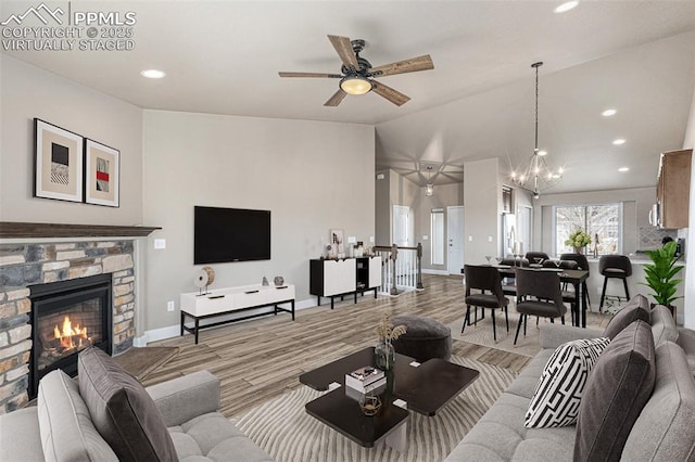 living room featuring a fireplace, light hardwood / wood-style flooring, ceiling fan with notable chandelier, and vaulted ceiling