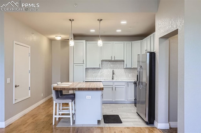 kitchen with butcher block counters, sink, decorative light fixtures, backsplash, and stainless steel fridge with ice dispenser