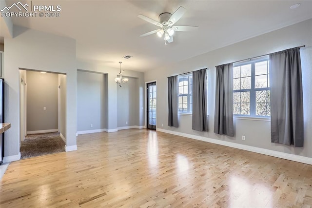 spare room with ceiling fan with notable chandelier and light hardwood / wood-style floors