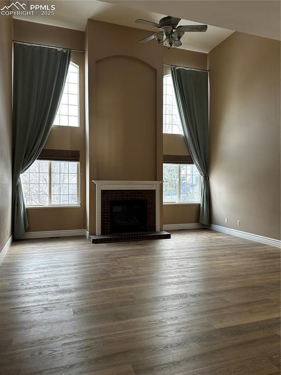 unfurnished living room with ceiling fan, a towering ceiling, a fireplace, and hardwood / wood-style floors