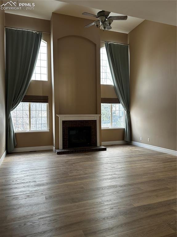 unfurnished living room featuring ceiling fan, wood-type flooring, a brick fireplace, and a high ceiling