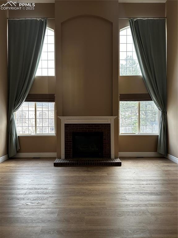 unfurnished living room with a brick fireplace, a towering ceiling, and light hardwood / wood-style flooring