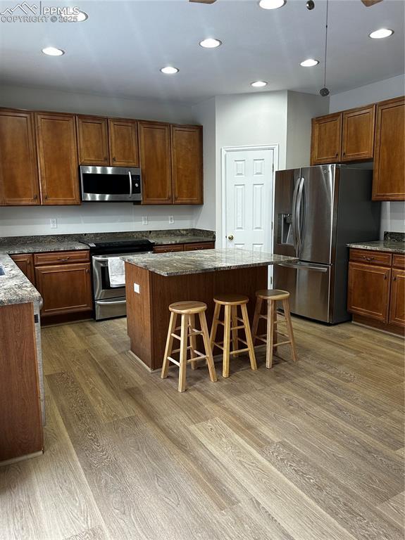 kitchen featuring a kitchen island, a kitchen bar, dark stone counters, stainless steel appliances, and dark wood-type flooring