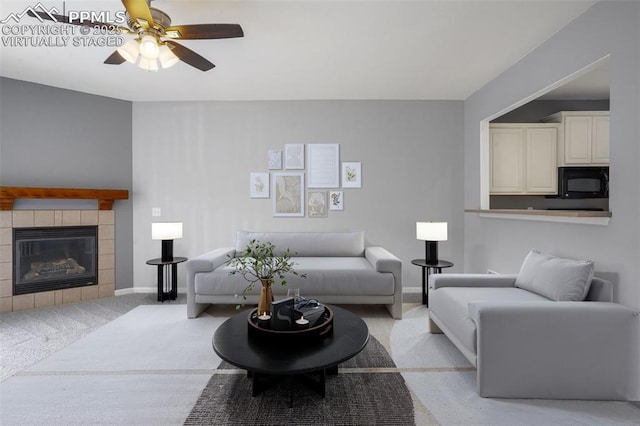 living room with ceiling fan, a tiled fireplace, and light carpet