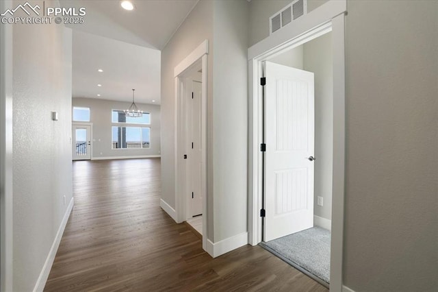 hall with a chandelier, dark wood-style flooring, visible vents, and baseboards