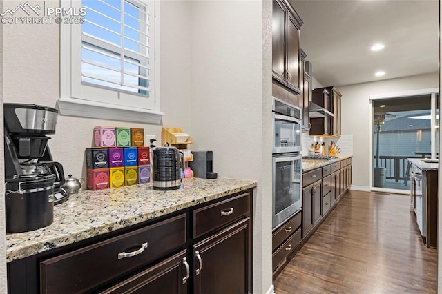 kitchen featuring tasteful backsplash, dark brown cabinetry, appliances with stainless steel finishes, dark wood-type flooring, and light stone counters