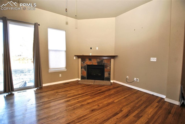 unfurnished living room featuring a stone fireplace and dark hardwood / wood-style floors