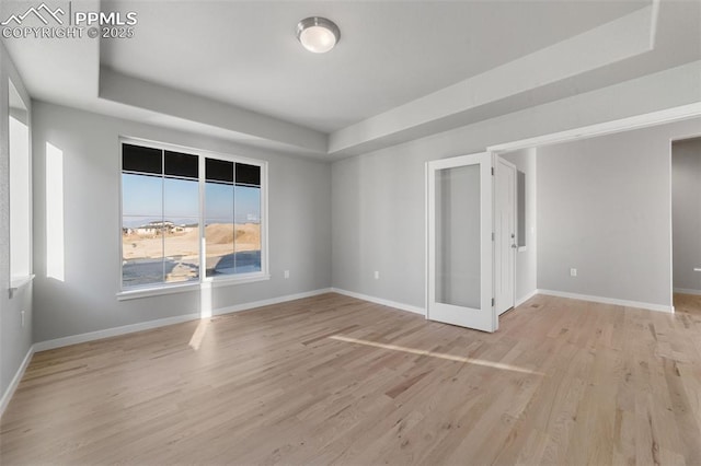 spare room featuring light wood-type flooring, french doors, and a tray ceiling