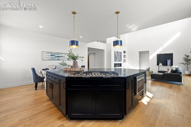 kitchen featuring pendant lighting, stainless steel gas stovetop, a kitchen island, and light hardwood / wood-style flooring