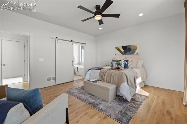 bedroom featuring ceiling fan, a barn door, connected bathroom, and light hardwood / wood-style floors