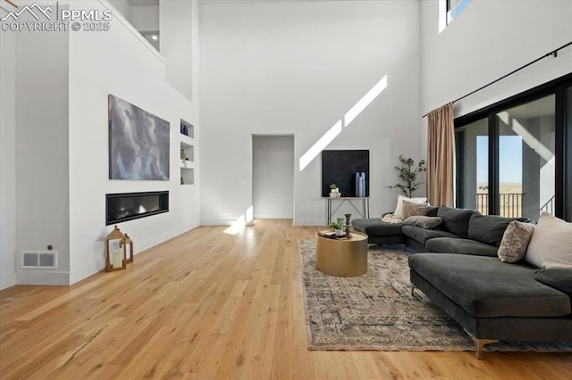 living room with built in shelves, a towering ceiling, a healthy amount of sunlight, and light hardwood / wood-style flooring