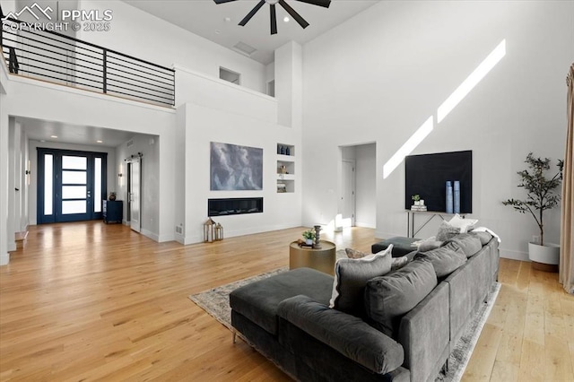 living room featuring a high ceiling, ceiling fan, and light wood-type flooring