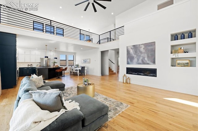 living room with ceiling fan, a towering ceiling, and light wood-type flooring