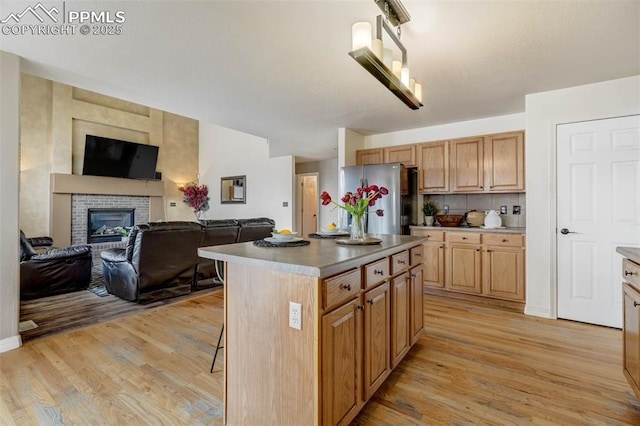 kitchen featuring tasteful backsplash, light hardwood / wood-style flooring, a fireplace, a center island, and stainless steel refrigerator