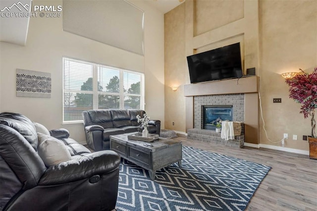 living room with hardwood / wood-style floors, a towering ceiling, and a brick fireplace