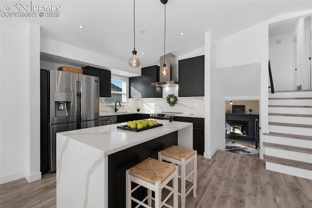 kitchen with appliances with stainless steel finishes, a kitchen island, wall chimney exhaust hood, sink, and decorative light fixtures