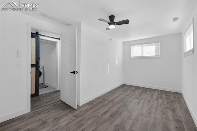 unfurnished room with ceiling fan, washer / dryer, a barn door, and hardwood / wood-style flooring