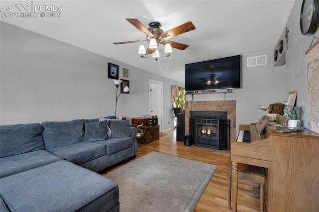 living room featuring ceiling fan, wood-type flooring, and a tile fireplace