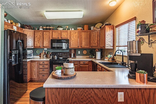 kitchen featuring kitchen peninsula, a textured ceiling, black appliances, light wood-type flooring, and sink