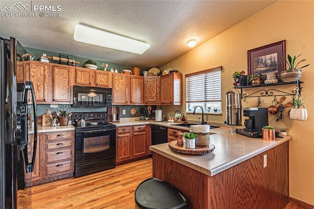 kitchen with black appliances, kitchen peninsula, a textured ceiling, light hardwood / wood-style flooring, and sink