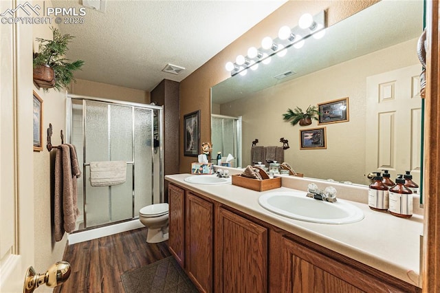 bathroom with toilet, a textured ceiling, hardwood / wood-style floors, a shower with door, and vanity