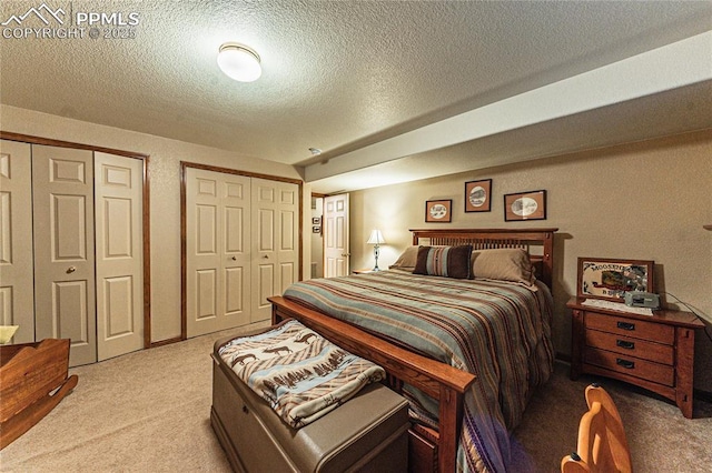 carpeted bedroom with a textured ceiling and multiple closets