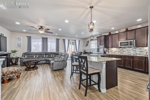 kitchen with light stone counters, hanging light fixtures, stainless steel appliances, an island with sink, and a breakfast bar