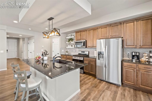 kitchen with stainless steel appliances, decorative light fixtures, light hardwood / wood-style floors, and sink