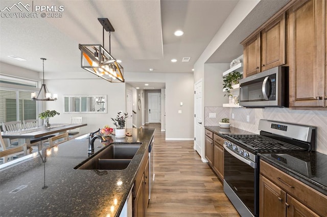 kitchen with stainless steel appliances, hanging light fixtures, sink, and dark stone counters