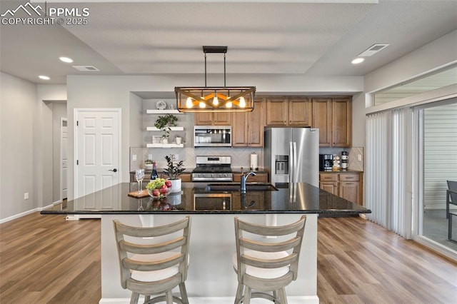 kitchen with sink, decorative light fixtures, hardwood / wood-style flooring, stainless steel appliances, and a kitchen island with sink