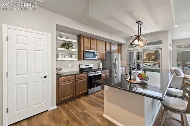 kitchen featuring dark wood-type flooring, hanging light fixtures, dark stone countertops, appliances with stainless steel finishes, and a kitchen breakfast bar