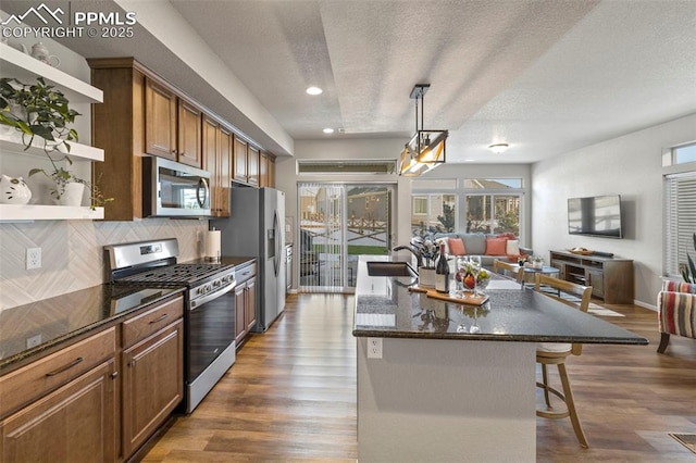 kitchen featuring pendant lighting, a kitchen bar, decorative backsplash, stainless steel appliances, and a center island with sink