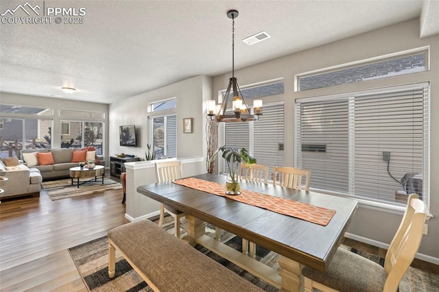 dining space with an inviting chandelier, wood-type flooring, and a textured ceiling