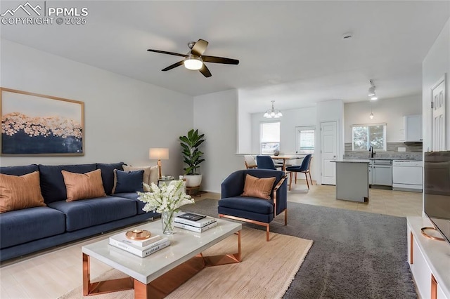 living room featuring sink, light wood-type flooring, and ceiling fan with notable chandelier