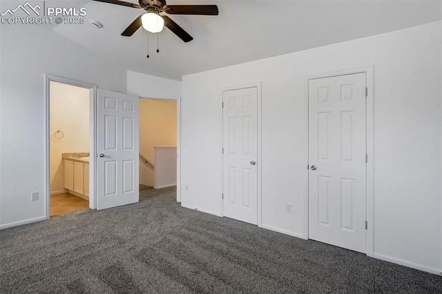 unfurnished bedroom with ensuite bathroom, dark carpet, multiple closets, and ceiling fan