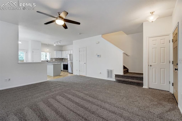 unfurnished living room with rail lighting, light carpet, and ceiling fan