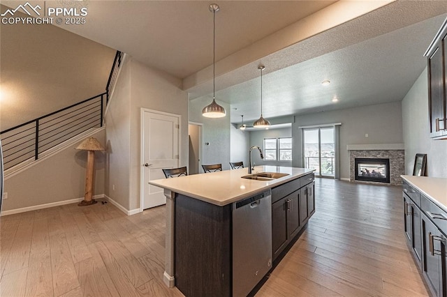 kitchen with dishwasher, pendant lighting, a center island with sink, sink, and a stone fireplace