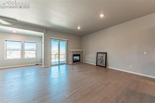 unfurnished living room featuring hardwood / wood-style floors, a textured ceiling, and a stone fireplace