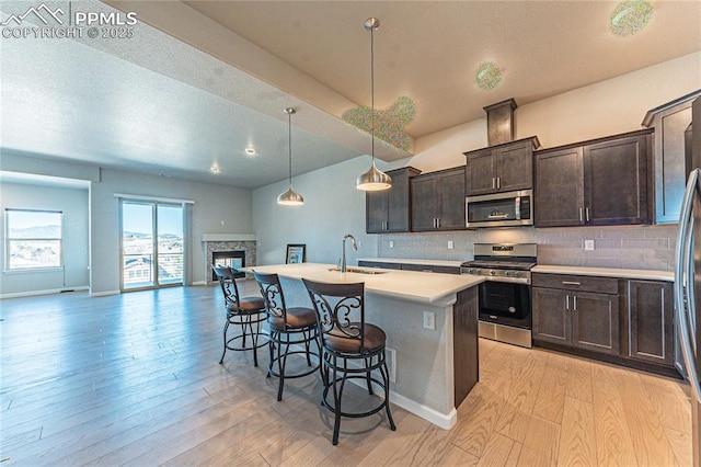 kitchen with stainless steel appliances, decorative backsplash, a kitchen island with sink, pendant lighting, and sink