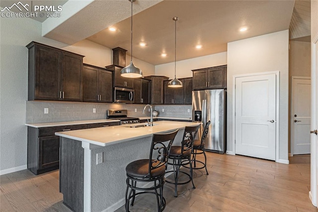 kitchen with pendant lighting, stainless steel appliances, an island with sink, sink, and dark brown cabinets