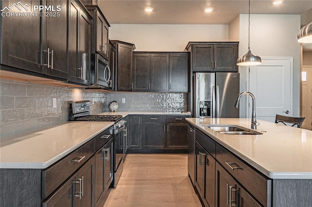 kitchen with pendant lighting, decorative backsplash, sink, an island with sink, and stainless steel appliances