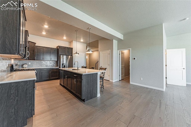 kitchen with stainless steel appliances, decorative backsplash, decorative light fixtures, a kitchen island with sink, and sink