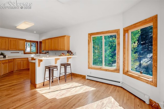 kitchen featuring kitchen peninsula, a baseboard radiator, light hardwood / wood-style flooring, and a kitchen bar