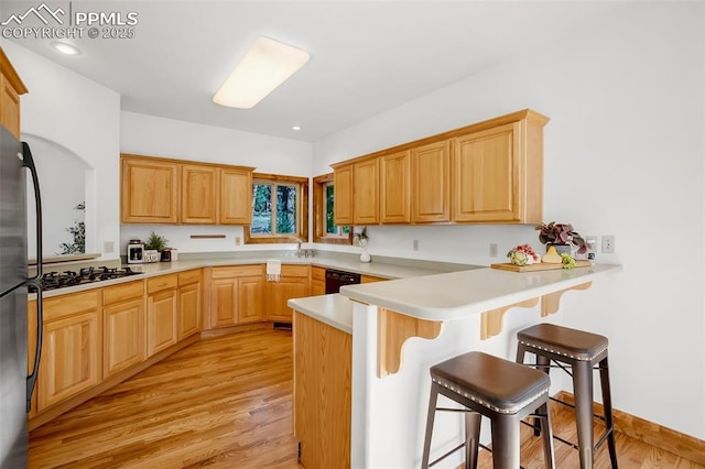 kitchen with gas cooktop, a kitchen breakfast bar, light hardwood / wood-style floors, kitchen peninsula, and stainless steel refrigerator