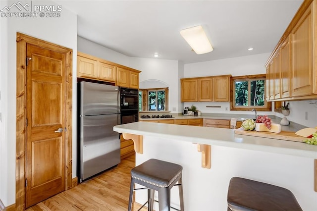 kitchen with light hardwood / wood-style floors, a kitchen breakfast bar, kitchen peninsula, and stainless steel refrigerator